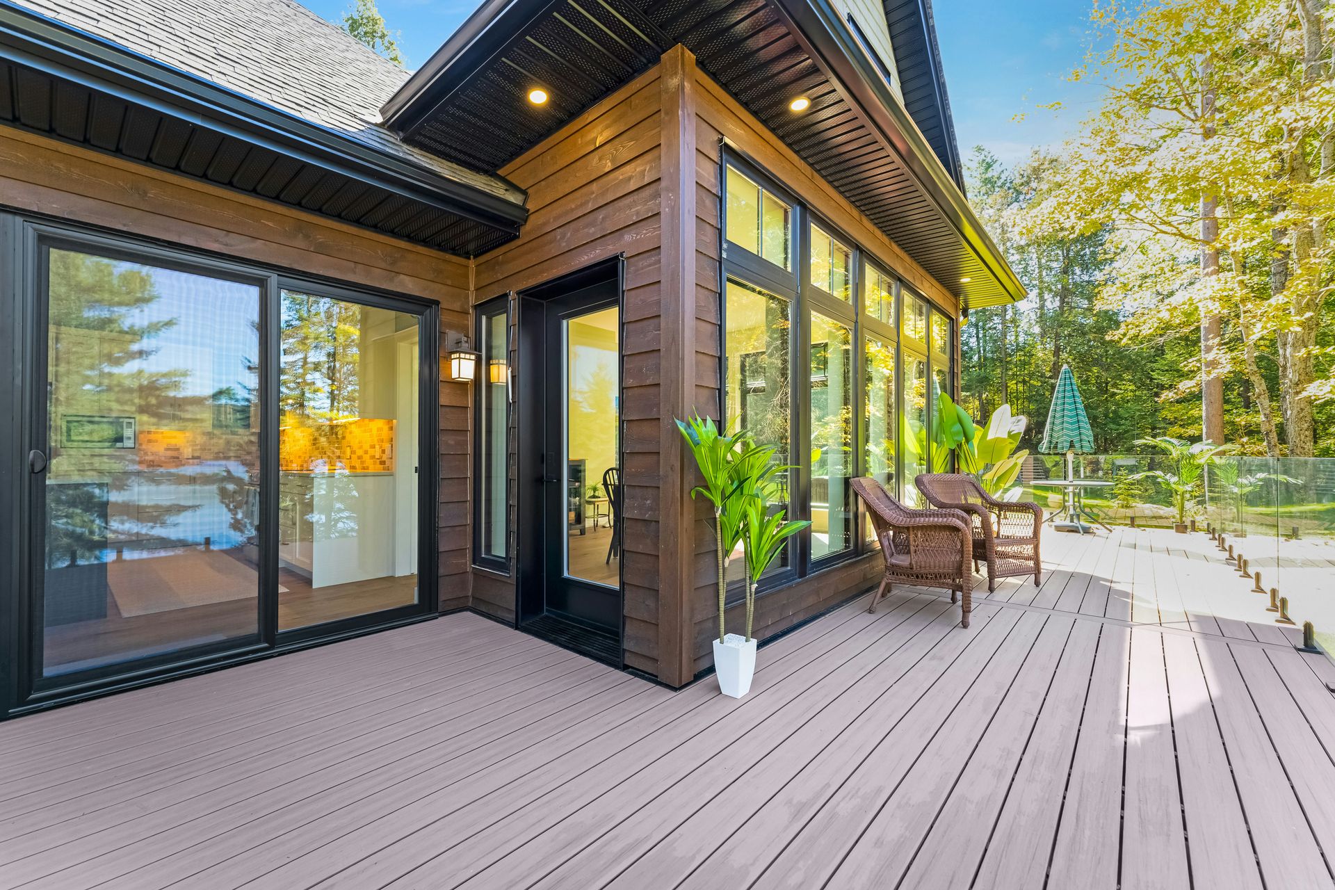 A wooden deck with wicker chairs outside a modern house in a forest