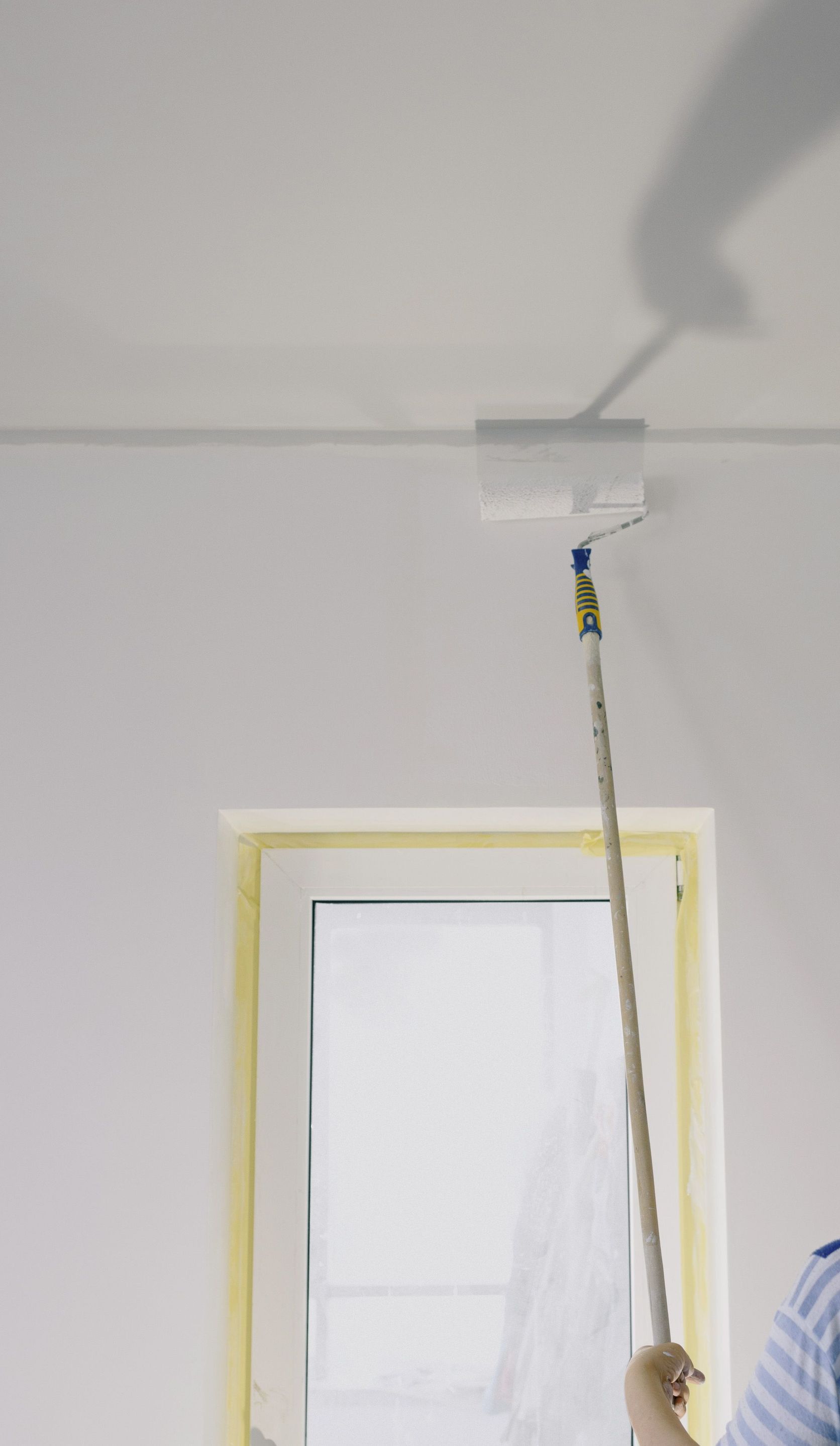 Crop faceless female holding paint roller and renovating walls in room at home
